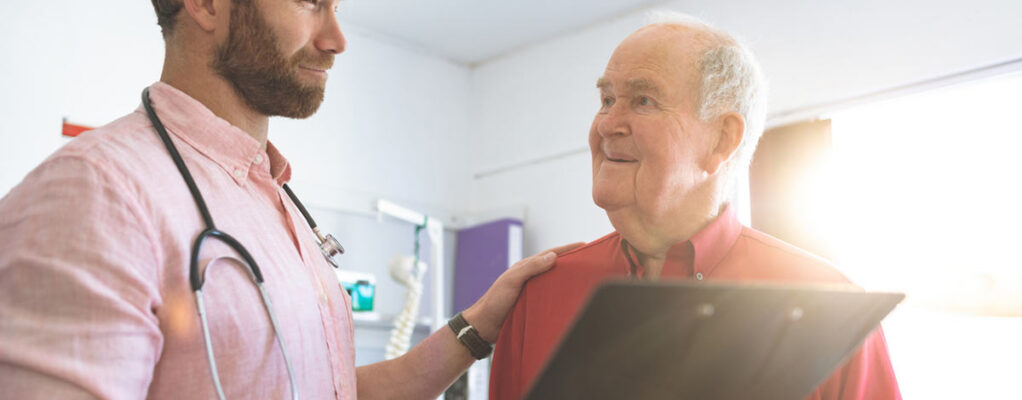 A male doctor puts his hand on the shoulder of an older male patient