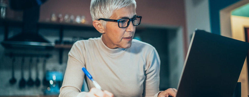 Woman looking at her laptop and writing with a pen and paper