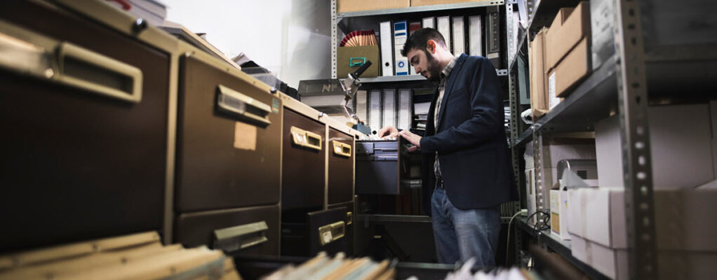 An office worker reviews a set of documents from a row of metal filing cabinets