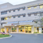 View of Fox Chase Cancer Center from its driveway. Fox Chase is a big, cream-colored hospital building.